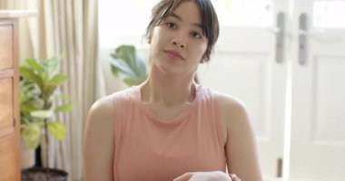 Asyalı kadın antrenmandan önce evde mavi yoga minderinde oturup akıllı telefondan antrenman saatini kontrol ediyor. Sağlık, rahatlama, farkındalık, sükunet, ev, fitness, iç mekan.