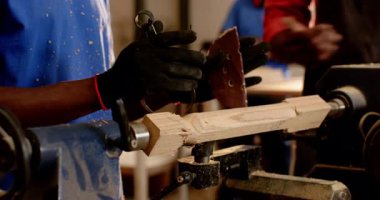 Torna tezgahında tahta boş, silindiri şekillendiren Afrikalı Amerikalı adam, pürüzsüz bir bitiriş için zımparalıyor. Sanatçılık, marangozluk, endüstriyel, zanaatkar, detay, atölye, hassasiyet