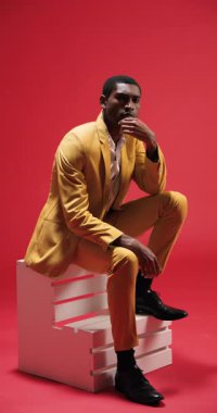 Dikey video: Modern beyaz sandalyede oturan şık sarı takım elbiseli kendine güvenen adam. Moda, tarz, zarafet, erkek, özgüven, iç mekan