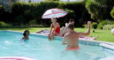 Çeşitli arkadaşlar şemsiye altında plaj topu atıyorlar, bardakları tokuşturuyorlar, akıllı telefon özçekimi pozu veriyorlar. Boş zaman, arkadaşlık, rahatlama, açık hava, hayat dolu, yaşam tarzı, yaz