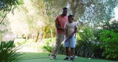 Afrikalı Amerikalı baba ve oğul arka bahçede golf öğretiyor, golf öğretiyor. Akıl hocalığı, aile, açık hava, boş zaman, eğlence, kaynaşma, doğal