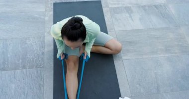 Kadın ayak etrafında direnç bandı takıyor, esneklik için veranda yoga minderinde bacak esnetiyor. Fitness, esneklik, açık hava, sağlık, aktif, egzersiz, dayanıklılık