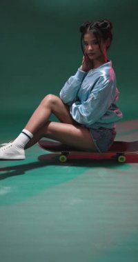 Dikey video: Stüdyoda kaykay yapan genç bir kadın, günlük kıyafetlerini giyiyor. Kaykay, moda, tarz, moda, giysi, sokak kıyafeti