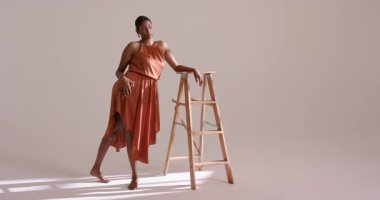 Paslı turuncu elbiseli, tahta merdivenlerde daireler çizen, stüdyoda oturan, saçları ayarlayan Hintli bir kadın. Zarafet, poz, moda, minimalist, stüdyo, profesyonellik, aydınlatma