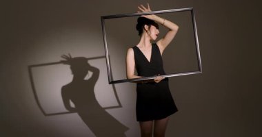 Asyalı Çinli kadın model stüdyoda siyah çerçeveyi kaldırıyor ve eğiyor. Minimalist, konsept, siluet, sanatsal, moda, monokrom, zarafet