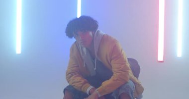 Stüdyonun puslu kaykayını kaldıran erkek kaykaycı ışıklı LED tüpleri vitrin güvertesini işaret ediyor. Çağdaş, karamsar, sinematik, kentsel, gençlik, dinamik, sanatsal