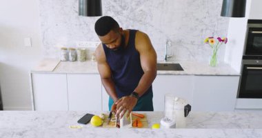 Afro-Amerikalı adam modern mutfakta meyve, blender ve akıllı telefonla taze meyve suyu hazırlıyor. Meyve suyu, mutfak, sağlıklı, ferahlatıcı, yaşam tarzı, aşçılık, modern