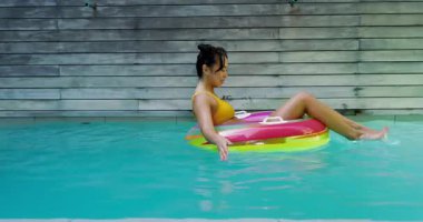 Çerçeveye giren Asyalı kadın arka bahçedeki havuzda yüzüyor ve tekmeliyor. Açık hava, boş zaman, hareketli, neşeli, sağlıklı, yaz, aktivite