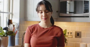 Asyalı kadın mutfakta mesaj okuyor, telefonu kaydırıyor, şaşırıyor ve gülümsüyor. Teknoloji, yaşam tarzı, modern, yerli, rahatlama, sağlık, farkındalık