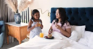 Afro-Amerikan kızı meyve suyunu yudumlarken Asyalı anne yatakta krep kesiyor. Aile, samimiyet, samimiyet, konfor, evcil, yetiştirme, çoklu nesil