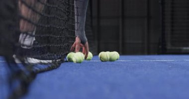 Tenis toplarını fark eden, erkek padel oyuncusu onları mavi sahada siyah raketle kepçeledi, kopyalama alanı. Spor, aktivite, atletizm, takım çalışması, hareket, eğlence, spor