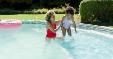 Anne ve kızı güven için rehberlik ettikten sonra arka bahçedeki havuzda denge ve tekme pratiği yapıyorlar. Aile, eğlence, su, güneşli, kaynaştırıcı, eğlenceli, güvenli