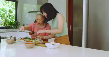 Hazırlandıktan sonra, son sınıf Çinli anne ve kızı mutfak adasında çubuklarla sos tadıyorlar. Aile, aile, aşçılık, işbirliği, canlı, geleneksel, sıcak