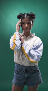 Dikey video: Şık ceketli genç bir kadın saçlarını düzeltiyor, stüdyoda güven içinde poz veriyor. Moda, güven, moda, yaşam tarzı