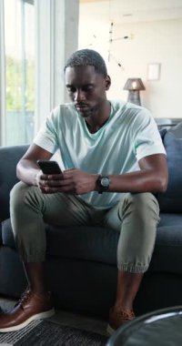 Dikey video: Düşünceli bir adam evdeki kanepede oturuyor, düşünüyor ve dinleniyor. Düşünceli, içsel, rahatlama, yalnızlık, tefekkür, sükunet.