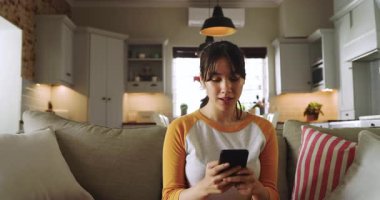 Asyalı bir kadın, evinde, kanepede akıllı telefonları kaydırıyor telefonu fırlatıp yatarken şaşırıyor. Rahatlama, rahatlama, gündelik, modern, rahat, yaşam tarzı, duygusal