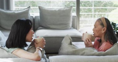 Asyalı Çinli anne ve kızı ellerinde kupalarla sohbet etmeye başladılar. Aile, bağ, iletişim, yaşam tarzı, konforlu, sıcak, jenerasyonel