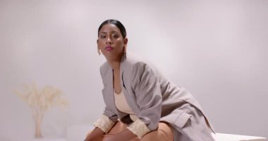 Stüdyoda çekim için modellik yapan Hintli kadın otlağın yanındaki bej blokta poz veriyor. Minimalist, moda, zarafet, kompozisyon, nötr, sakin, sofistike