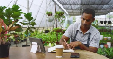 Serada, tablet ve defter kullanan bir adam, fabrika fidanlığını yönetiyor. Tarım, tarım, teknoloji, girişimci, bahçıvanlık, sürdürülebilirlik