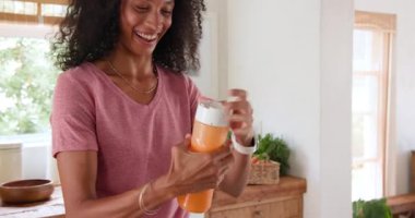 Parlak mutfakta taze portakal suyunu bardağa dolduran kadın evde mutlu bir şekilde gülümsüyor. İçecek, narenciye, ferahlatıcı, kahvaltı, sağlıklı, yaşam tarzı