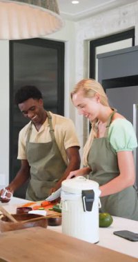 Dikey video: Genç çift modern mutfakta birlikte yemek pişiriyor, taze malzemeleri mutlu bir şekilde hazırlıyorlar. Mutfak, yemek hazırlama, takım çalışması, yaşam tarzı
