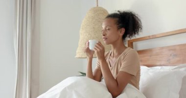 Kadın yatakta dinleniyor, kahvesini içiyor ve akıllı telefonuna bakıyor, evde. Rahatlama, sabah, rahat, teknoloji, yaşam tarzı, ev