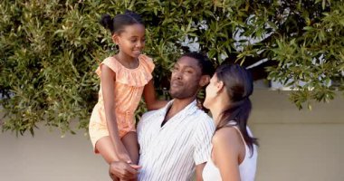 Gülümseyen Afrikalı Amerikalı baba kızını tutarken anne ağacın altında gülüyor. Çeşit çeşit aile, bağ, doğa, mutluluk, neşe, birliktelik