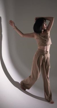 Dikey video: Modern moda stüdyosunda kendine güvenen şık bej elbiseli bir model. stil, giysi, moda, zarafet, fotoğraf çekimi, giysi