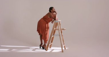 Güneş ışığı sistemi Hintli kadını stüdyoya çekiyor ve merdivende turuncu elbiseyle poz veriyor, kopyalama alanı. Minimalist, çağdaş, estetik, aydınlatma, moda, zarafet, duruş