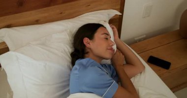 Pijamalı bir kadın evinde, komodininde akıllı telefonuyla yatakta huzur içinde uyuyor. Rahatlama, uyku zamanı, konfor, teknoloji, dinlenme, sükunet