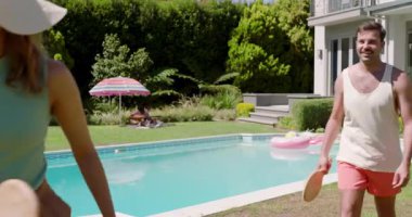 Beyaz adamdan el altından top fırlatmaya başlayarak havuz kenarında havuz başı fotokopi alanında birkaç raket toplanıyor. Eğlence, eğlence, açık hava, etkinlik, spor, modern yaşam tarzı.