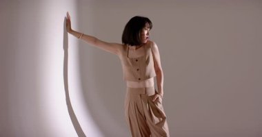 Çinli bir kadın model, fotoşoplar sırasında kıvrımlı stüdyo duvarına sol elini koyuyor. Minimalist, zarif, moda, güzellik, portre, stüdyo, sofistike