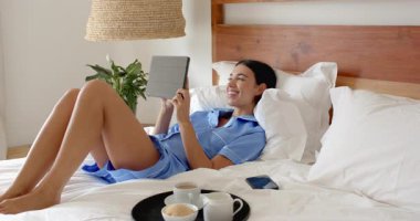 Yatakta dinlenirken, pijamalı bir kadın evde kahvesini yudumlarken. Rahatlama, rahatlama, yaşam tarzı, teknoloji, sabah, rahatlık