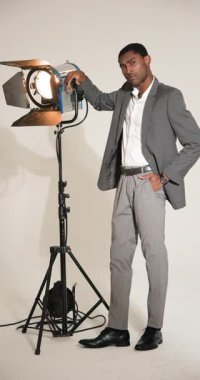Dikey video: Gri takım elbiseli kendine güvenen adam stüdyo ışığını moda fotoğrafçılığında ayarlıyor. Fotoğraf, profesyonel, ekipman, ışıklandırma, stil, yaratıcılık