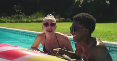Beyaz kadın girdap şeklinde yüzerken, siyah adam güneşli arka bahçe havuzunda yüzüyor. Oyun, samimiyet, boş zaman, açık hava, rahatlama, yaz, canlı