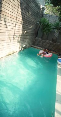 Dikey video: Genç kız havuzda dinleniyor, güneşli bir öğleden sonranın keyfini çıkarıyor. Yaz, rahatlama, rahatlama, yüzme, tatil, eğlence.