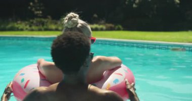 Yüzen akıntıyı fark eden, çeşitli çiftler gülüyor, sohbet ediyor ve arka bahçedeki havuzda tüp yerleştiriyor. Tatil, boş zaman, yaz, mahremiyet, şakacı, rahatlatıcı, hayat dolu.