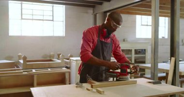 Picking up orbital sander, African American carpenter sanding plank at workshop smoothing surface. Craftsmanship, woodworking, power tools, workshop, renovation, carpentry, hands-on