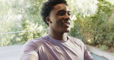 Yirmili yaşlarda Afro-Amerikalı bir adam elinde kamerayla terasta havuz yeşili gösteriyor. Gündelik, açık hava, boş zaman, yaşam tarzı, canlı, doğal, gençlik