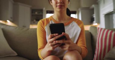 Tebligat geliyor, 20 'li yaşların ortasında Asyalı bir kadın evinde oturmuş telefonda cevap yazıyor. Rahatlama, iletişim, teknoloji, ev, yaşam tarzı, sıcak aydınlatma, gündelik