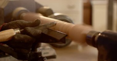 Eldiven çeviren erkek keski kaldırıyor. Tahta torna şekillendirme kanallarında dönmeye başlıyor. Kopya uzayı. Sanatçılık, marangozluk, zanaat, kesinlik, zanaat, geleneksel, atölye