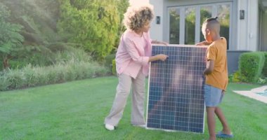 Güneş, Afro-Amerikan ailesini avluda güneş paneli taşıyarak en iyi güneş ışığı için hizaya sokuyor. Sürdürülebilirlik, yenilenebilirlik, çevre dostu, açık hava, modern, bağlantı, eğitim