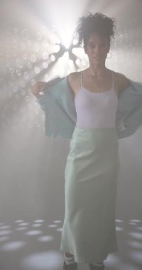 Dikey video: neşeyle dans eden, şık giyinmiş bir kadın canlı stüdyo ışıklarının tadını çıkarıyor. Dans, moda, hareket, renkli, gece hayatı, enerji