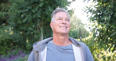 Gülümseyen olgun bir adam yemyeşil bahçe ortamında huzurlu bir sabahın tadını çıkarıyor. Rahatlama, açık hava, doğa, yeşillik, yaşam tarzı, rahatlık.