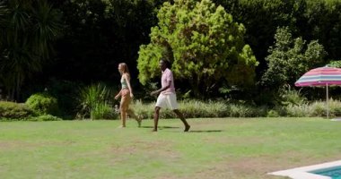 Gevşek futbol topunun tetiklediği, çeşitli arkadaşların eğlenmek için havuzun yanındaki çimlerde top sürüp pas atması. Açık hava, boş zaman, aktivite, yaşam tarzı, canlı, gündelik, yoldaşlık