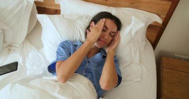 Mavi pijamalı bir kadın yatağında akıllı telefonuyla uyanıyor, evde. Sabah, rahatlama, yaşam tarzı, teknoloji, yatak odası, uyanış.