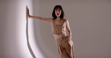 Sıraları takip eden bronz elbiseli Çinli kadın spot ışıklarına basıyor, gri duvara yansıyor. Portre, moda, minimalist, zarafet, profesyonel, tarz, güven