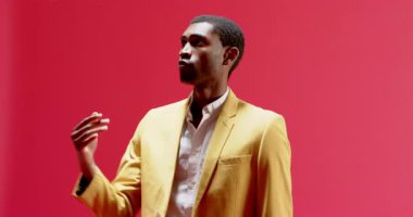 Siyah ceketli Afro-Amerikalı adam kırmızı arka plana karşı elini kaldırarak altın küre takip uçuşu yapıyor. Minimalist, dinamik, odaklanma, zarafet, profesyonellik, stüdyo, canlı