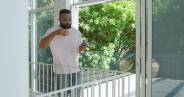 Modern uzayda, elinde kahve fincanı tutan, akıllı telefonları dinleyen Afro-Amerikan bir adam. Çağdaş, yaşam tarzı, üretkenlik, yeşillik, kahve, gündelik, teknoloji