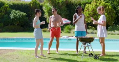 Diverse friends toasting by pool grabbing tongs at charcoal grill dancing as music starting up. Outdoor, leisure, celebration, summer, socializing, relaxation, vibrant